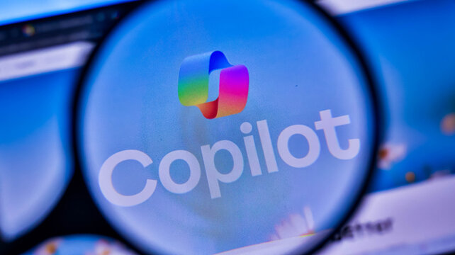 Magnifying glass focused on copilot logo on screen showing tech.