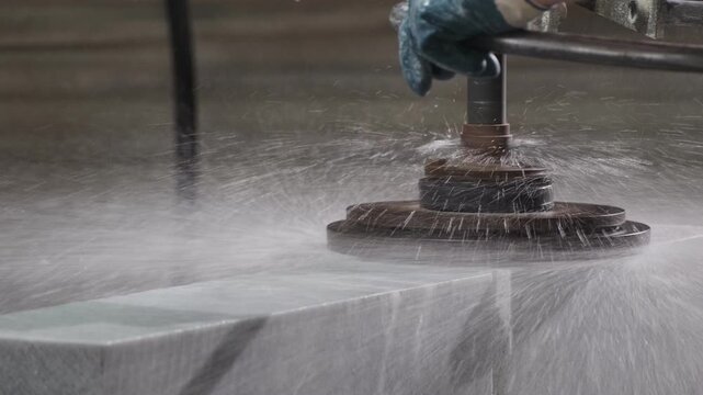 Industrial worker polishing a marble slab with a wet grinding machine in a factory. Water spraying during the process