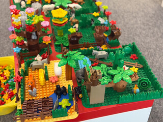 Fototapeta premium Colorful lego-style toy jungle scene with animals, trees, flowers, and small buildings on a play table