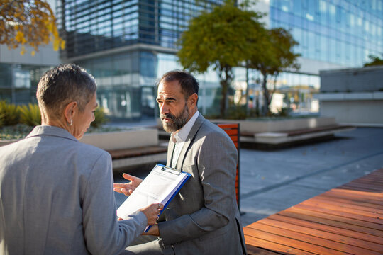 Two senior business professionals discussing financial report outside office