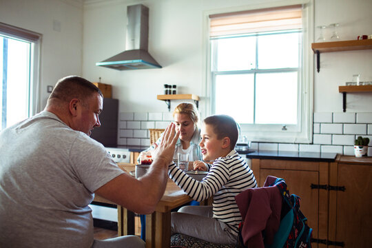 Father and son high five at breakfast in home kitchen