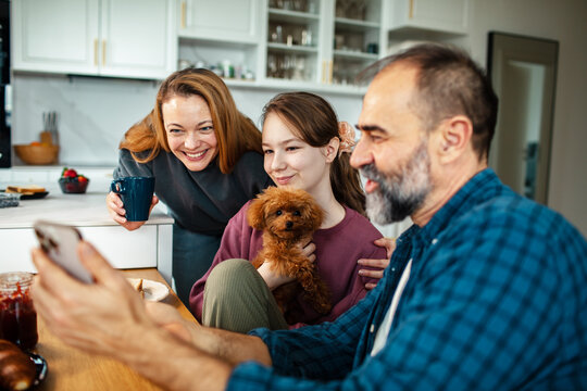 Parents and teen daughter with puppy using smartphone in kitchen