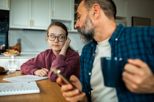 Father and teen daughter studying together at home kitchen table