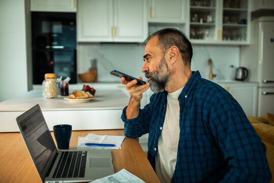 Middle-aged man using voice assistant while working from home kitchen