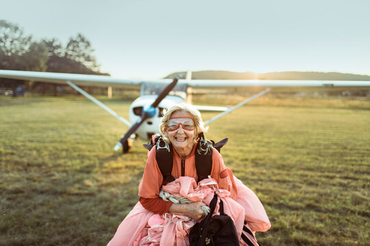 Happy senior woman skydiver with parachute by small airplane at sunset