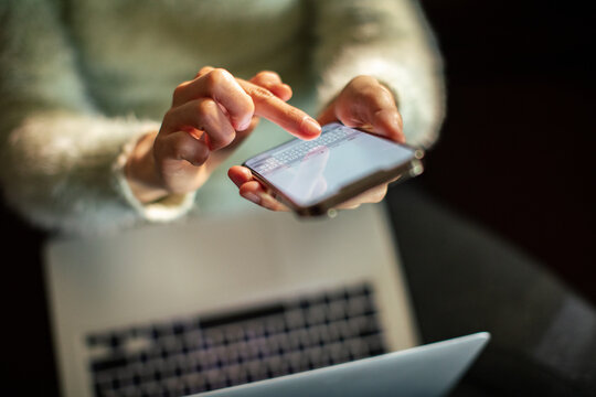Person texting on smartphone while working on laptop at home