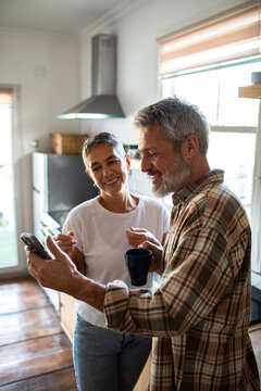 Smiling mature couple using smartphone in bright home kitchen