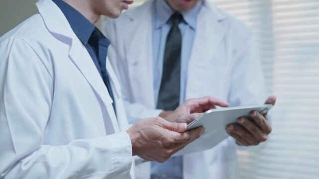 Doctors discussing a medical case together in a modern clinic office, using a tablet and laptop for telehealth, healthcare technology, medical consultation and health insurance planning.