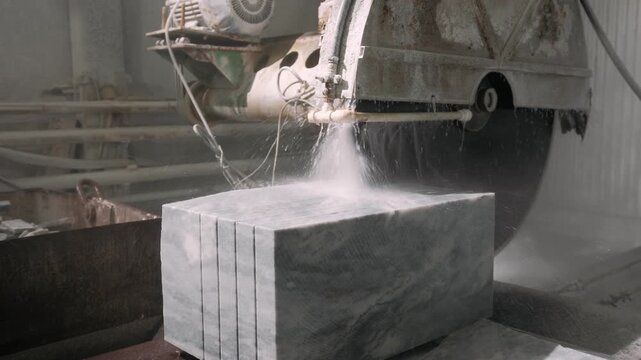 Industrial circular saw machine cutting marble block with water cooling in a stone processing factory