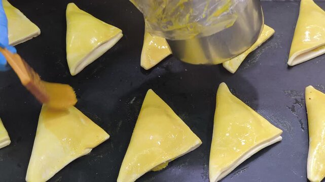 Close-up of puff pastry turnovers being brushed with egg wash for a golden finish