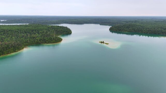 Aerial view of a picturesque sandy island surrounded by vibrant turquoise water on Big Skunk Lake in northern Ontario, with pristine boreal forest and the expansive lake in the background.
