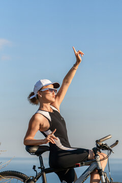 Cyclist woman point, outdoor sport training posing with bicycle at sunset showing a relaxed lifestyle during sunny summer outdoor vacation