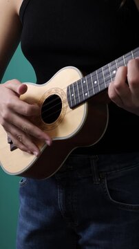 Ukulele player strumming chords against teal studio backdrop, close-up
