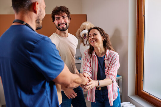 Veterinarian shaking hands with happy pet owners and dog
