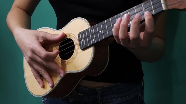Ukulele player strumming chords against a teal studio backdrop