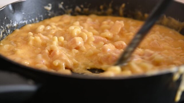Homemade mac and cheese being stirred in a skillet