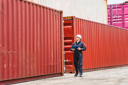 Male logistics engineer walking and inspecting stacked shipping containers