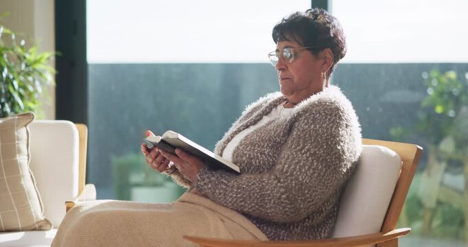 Elderly, woman or reading with book for literature, scripture or knowledge in retirement home. Senior, female person or relax with glasses, story or novel for information, learning or study in house