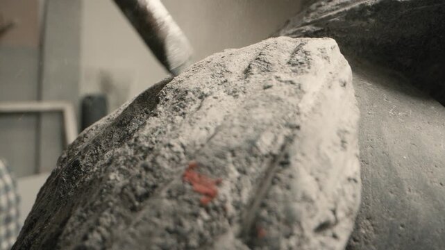 Sculptor uses pneumatic chisel on stone in artist workshop to create texture and form during the carving process