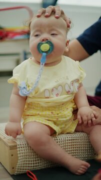 Baby engaging in a physical therapy session, receiving assistance with a pacifier from a therapist for developmental support