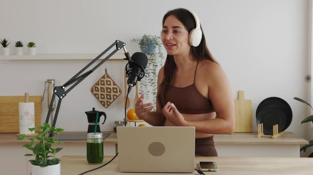 Charismatic female content creator speaking into a professional microphone, hosting a live audio broadcast or podcast about nutrition and healthy lifestyle from her modern kitchen studio