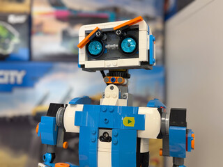 Fototapeta premium Close-up of a blue and white lego robot toy with bright eyes on a blurred indoor background.