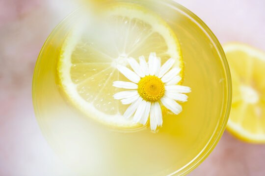 Close-up macro view of a fresh lemon slice floating in a bright yellow citrus drink with a white chamomile flower. Top view. Perfect for healthy drinks, wellness, detox, lemonade, herbal tea