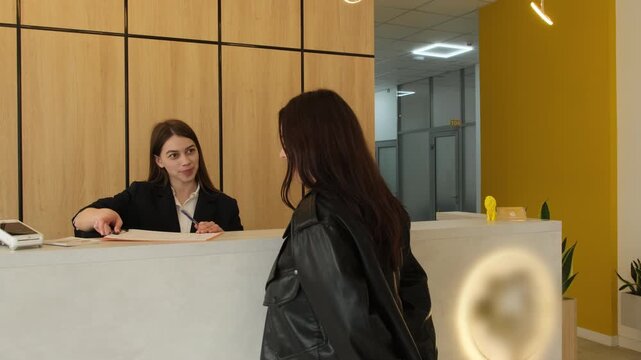 Administrator carefully gives woman registration form and high-quality pen before consultation. Woman explains registration procedure. Slow motion
