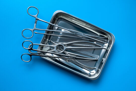 Sterile surgical instruments and tools - scalpels, scissors and others - in a stainless tray on blue background, top view