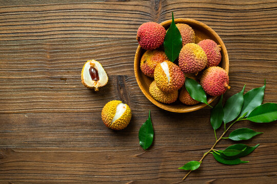 Fresh lychee fruit in bowl with green leaves, top view