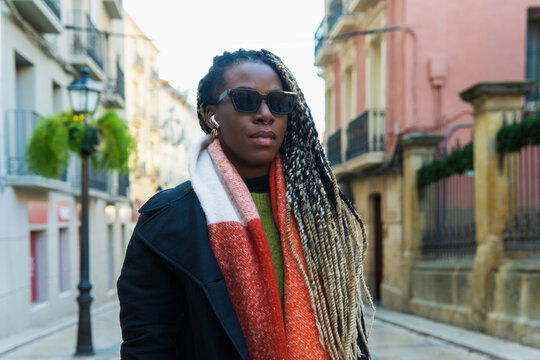 Black woman wearing sunglasses and colorful scarf walking in city