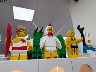Obraz premium Colorful lego minifigures lined up on a store shelf, including a chicken costume, bunny, and other playful characters under bright indoor lights.