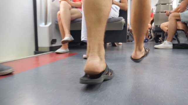 Male legs going through modern wagon of train during travel. Feet of young man walking along carriage of passenger railway transport. Concept of summer vacation or holiday. Low view