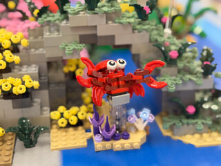 Fototapeta premium Red toy crab on a colorful lego underwater scene with rocks, flowers, and blue water