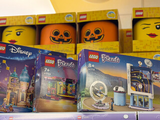 Fototapeta premium Colorful lego toy boxes displayed on a store shelf with disney and friends sets, with halloween pumpkin faces in the background