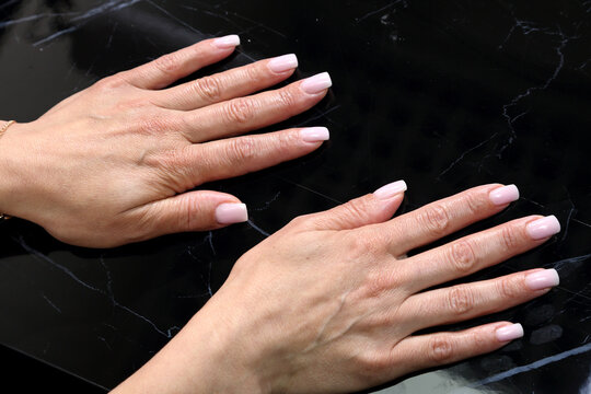 Receiving Professional Manicure in Modern Salon. Beautiful, well-groomed women's hands with elegant nails against a dark background. Beauty salon concept: manicures, pedicures. 