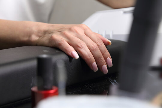 Receiving Professional Manicure in Modern Salon. Beautiful, well-groomed women's hands with elegant nails against a dark background. Beauty salon concept: manicures, pedicures. 