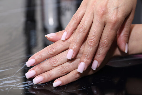 Receiving Professional Manicure in Modern Salon. Beautiful, well-groomed women's hands with elegant nails against a dark background. Beauty salon concept: manicures, pedicures. 