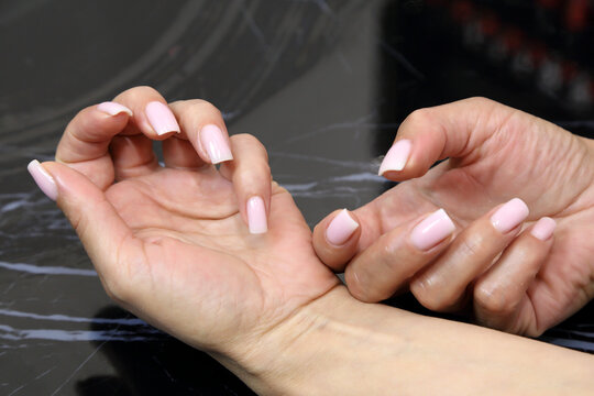 Receiving Professional Manicure in Modern Salon. Beautiful, well-groomed women's hands with elegant nails against a dark background. Beauty salon concept: manicures, pedicures. 