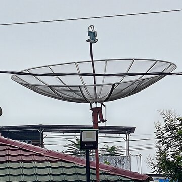 A large parabolic satellite dish installed above rooftops, used for satellite communication under an overcast daytime sky.