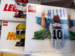 Fototapeta premium Lego toy boxes on a store shelf, including lionel messi celebration set and formula 1 race car packs, displayed in a retail aisle.