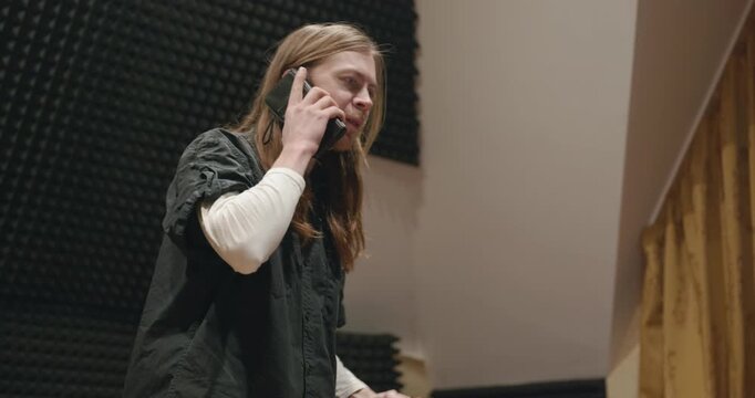 Caucasian man talk by phone and drink hot water in home sound recording studio. Single male is drinking tea in evening. 4K 10-bit
