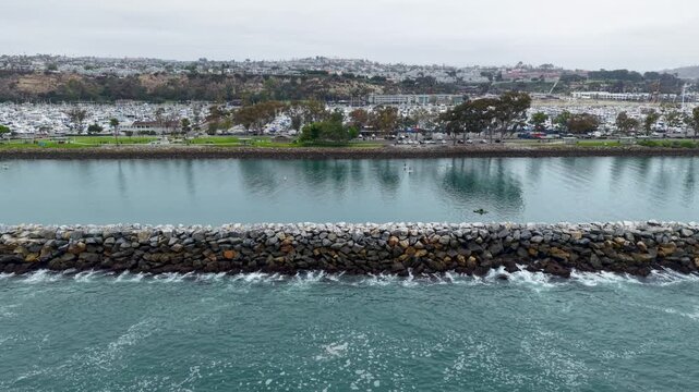 A slow leisurely Low Altitude drone shot of the Jetty at Dana Point. The drone is positioned over the Pacific Ocean side of the jetty looking into the Harbor. Slowly drifting side to side.