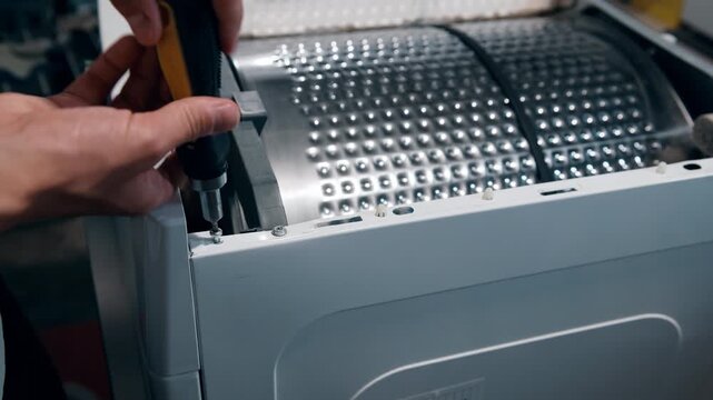 Close-up of screws being removed from the side panel of a tumble dryer, taking the machine apart for repair. A DIY appliance service detail &ndash; loosening the fasteners to open up the housing.