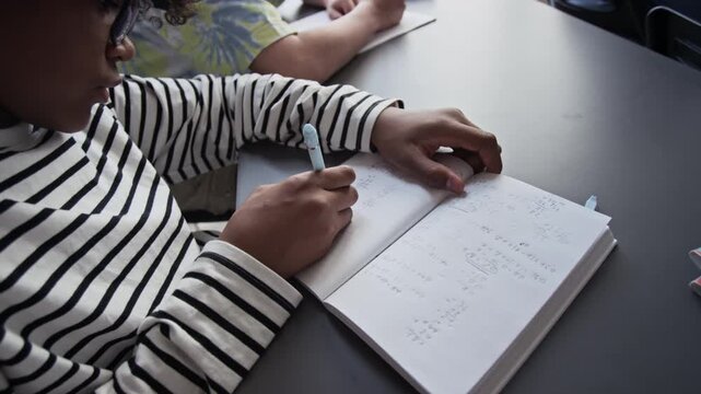 African American teenager writing math equations in notebook during school class. Footage for educational marketing, tutoring services, and school enrollment campaigns