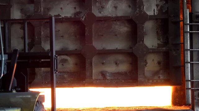 Heavy machinery extracts glowing hot steel slabs from an industrial furnace for thermal processing. This process maintains high temperature standards within a controlled metal fabrication facility.