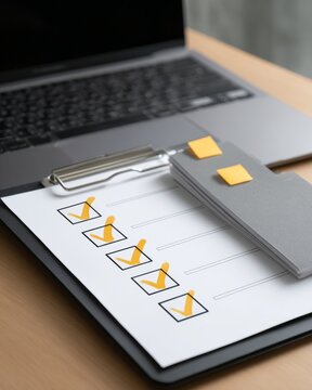 Checklist on clipboard with check marks beside gray folder and laptop on wooden desk