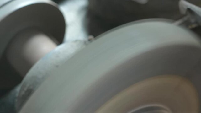 A worker uses a motorized abrasive wheel to grind and sharpen raw steel blades by applying pressure to the metal edge, which generates intense sparks during the industrial maintenance task.