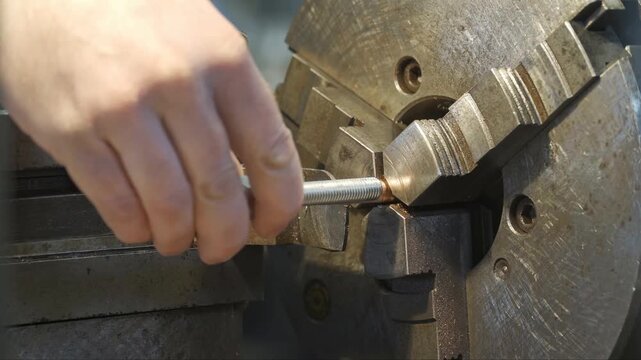 Industrial metal lathe machinery utilizes a rotating chuck to hold and shape cylindrical brass rod components with cutting tools to produce precise metallic parts for various manufacturing projects.