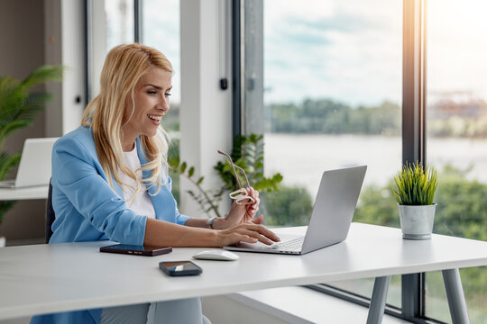 Smiling Caucasian businesswoman working on laptop in modern bright office with river view